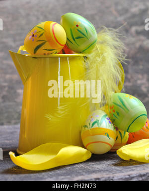 kleine gelbe Gießkanne mit Ostern Eiern auf hölzernen Hintergrund Stockfoto