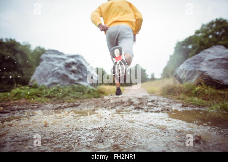 Mann durch Schlammpfützen Joggen Stockfoto