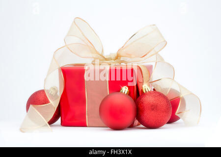 Ein roter Weihnachtsgeschenk mit Goldband und rote Baumschmuck isoliert auf einem weißen Hintergrund. Stockfoto