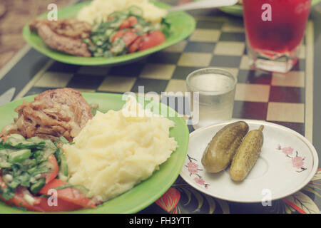 Salz, Kartoffeln, gebratenes Fleisch, Gurken, Salat von frischen Gurken und Tomaten. Sehr leckeres Essen auf dem Teller. Stockfoto