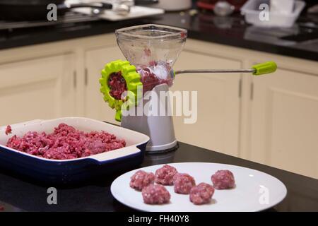 Ein Fleischwolf oder Schleifmaschine ist auf rohes Rindfleisch verwendet wird, die Zutaten für Frikadellen in einer Familie Landhausküche vorbereitet. Stockfoto