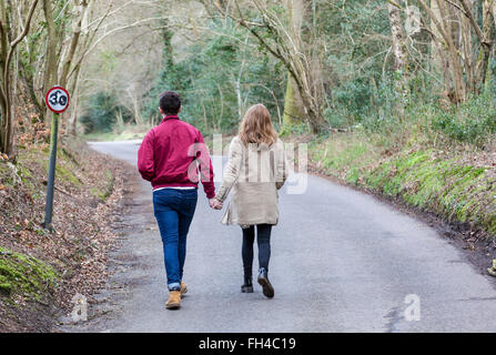 Junges Paar gehen weg hand in hand entlang einer von Bäumen gesäumten Landstrasse im zeitigen Frühjahr, Surrey, England. Stockfoto