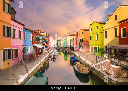 Ein Blick auf die bunten Häuser in Burano im Laufe des Tages am Kanal entlang. Bunte Wolken am Himmel zu sehen. Stockfoto