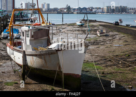 Ein altes Fischerboot sitzt auf der Schlammbank bei Ebbe in Portsmouth Harbour mit der Skyline von Gosport in der Ferne. Stockfoto