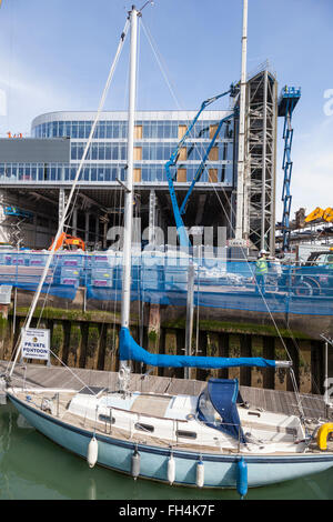 Eine kleine Yacht Liegeplatz neben einem Holzponton in Camber Dock Sir Ben Ainslie Land Rover BAR Gebäude in den Schatten gestellt. Stockfoto