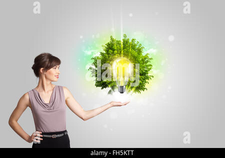 Junges Mädchen präsentieren Idee Glühbirne mit grüner Baum Stockfoto