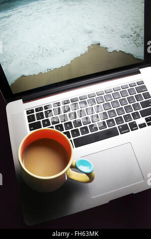 Kaffeebecher auf Laptop-Computer mit Strand auf Bildschirm Stockfoto