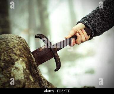 Hand des tapferen Ritters versucht, das magische Schwert Excalibur in den Stein zu entfernen Stockfoto