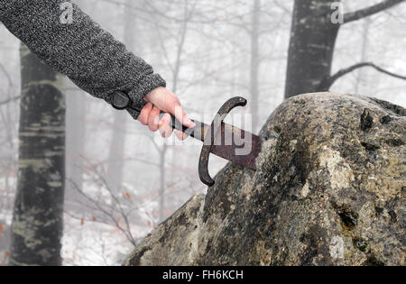 Hand des tapferen Ritters versucht, das magische Schwert Excalibur in den Stein zu entfernen Stockfoto