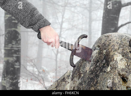 Hand des tapferen Ritters versucht, das magische Schwert Excalibur in den Stein zu entfernen Stockfoto