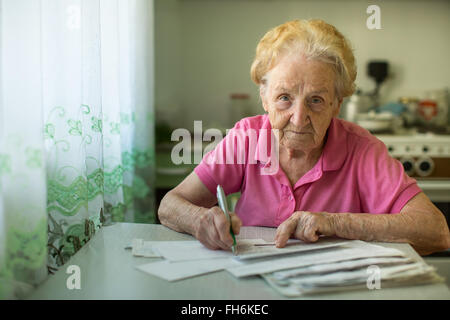Die alte Frau füllt Stromrechnungen in der Küche sitzen. Stockfoto