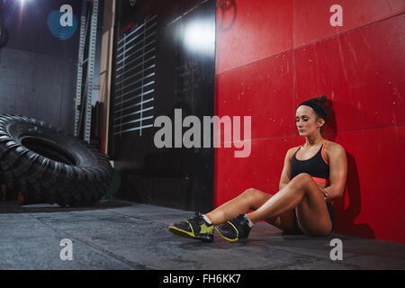 Fit Woman in Active-Wear sitzen auf dem Boden gegen die Wand im Fitness-Studio Stockfoto