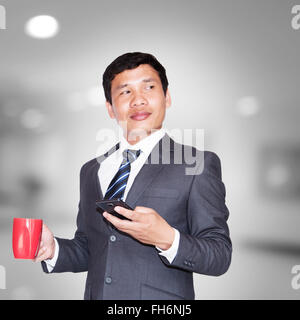 Asiatische Geschäftsmann mit Kaffee und mit Smartphone wegsehen auf Leerzeichen Stockfoto