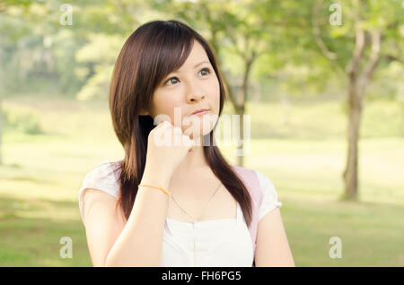 Junge asiatische Mädchen Studentin steht auf dem Campus Rasen, einen Gedanken und lächelnd. Stockfoto