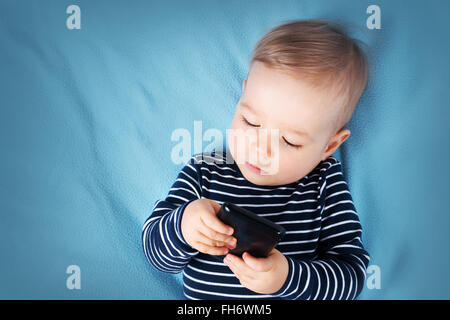 kleiner Junge auf blaue Decke Hintergrund mit Handy Stockfoto