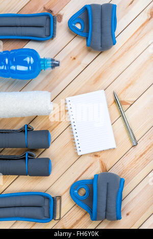 Fitness-Geräte. Hanteln, Fussblei, Handgelenk Gewichte, Handtuch, isotonisches Getränk und Notebook zu Trainingsplan auf Brettern. Stockfoto