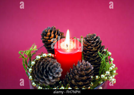 Die dekorativen Weihnachts Komposition aus roten Kerze, Tannenzapfen auf rotem Hintergrund Stockfoto