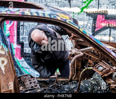Güterbahnhof Bahnhof Pankow, Berlin. Alter Mann schaut ausgebrannte Auto in Brand beschädigt Garage am stillgelegten Güterbahnhof Schiene Stockfoto