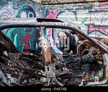 Güterbahnhof Bahnhof Pankow, Berlin. Alter Mann schaut ausgebrannte Auto in Brand beschädigt Garage am stillgelegten Güterbahnhof Schiene Stockfoto