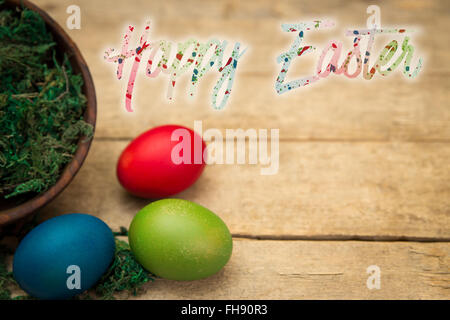 drei farbige Eiern auf einem hölzernen Hintergrund und Text Frohe Ostern Stockfoto