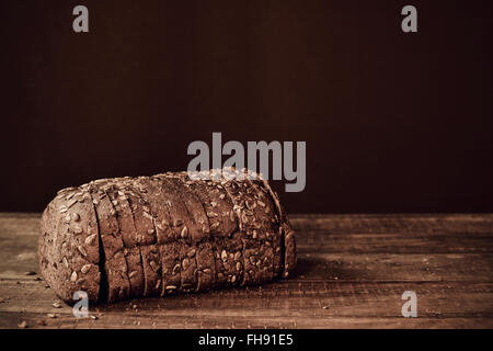 eine in Scheiben geschnittene Laib Roggenbrot mit Sonnenblumenkernen auf einer rustikalen Holzoberfläche in Sepia-Tonung gekrönt Stockfoto