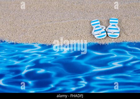 Blaue Spielzeug Flip-Flops am Konzept Strand mit Sand und Wasser-Folie Stockfoto