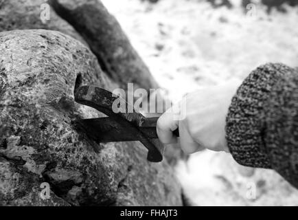 Hand des tapferen Ritters versucht, das magische Schwert Excalibur in den Stein zu entfernen Stockfoto