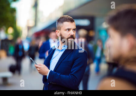 Hipster-Manager mit einem Smartphone außerhalb in belebten Straße Stockfoto