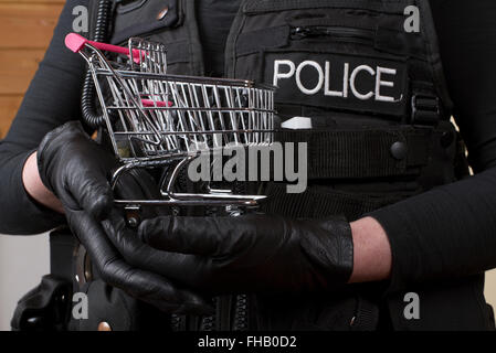 Polizist hält einen kleinen Einkaufswagen im Konzept der Ladendiebstahl Stockfoto