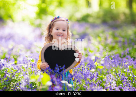 Kleine Mädchen spielen im blühenden Garten. Baby auf Osterei jagen in blue Bell Blumenwiese. Kleinkind Kind Kommissionierung Glockenblume Stockfoto