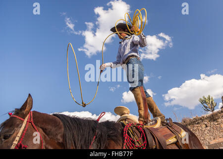 Eine mexikanische Charro oder Cowboy Praktiken Abseilen Fähigkeiten auf seinem Pferd vor einem Charreada Wettkampf auf einer Hacienda-Ranch in Alcocer, Mexiko. Die Charreada ist eine traditionelle mexikanische Rodeo und testet die Fähigkeiten des Cowboys reiten, Abseilen und Vieh zu kontrollieren. Stockfoto