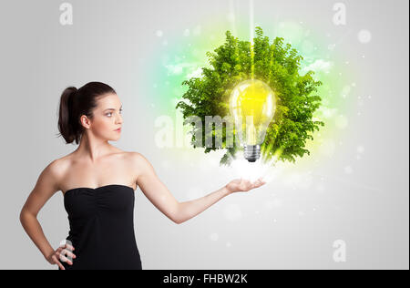 Junges Mädchen präsentieren Idee Glühbirne mit grüner Baum Stockfoto