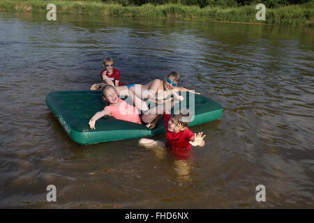 Kinder im Alter von 12 bis 8, die spielen auf einer Luftmatratze am Fluss Pilica. Rzeczyca Zentralpolen Stockfoto