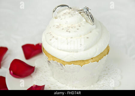 Trauringe in Cupcake Icing mit Sterne Streusel und rote Rosenblüten. Stockfoto