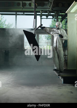 Ansicht eines Arbeitnehmers einen vollen weißen Schutzanzug tragen und Atmung Maske, Sand strahlen eine Metall-Kiste hing an einem metallischen Strahl in Stockfoto