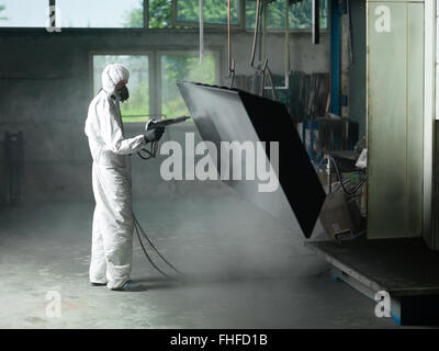 Ansicht eines Arbeitnehmers einen vollen weißen Schutzanzug tragen und Atmung Maske, Sand strahlen eine Metall-Kiste hing an einem metallischen Strahl in Stockfoto