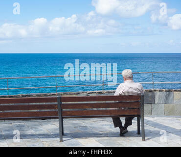 Alter Mann sitzt auf der Bank, Blick auf das Meer in Spanien Stockfoto