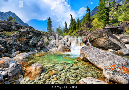 Klares Wasser aus einem Gebirgsbach und ein kleiner Wasserfall in einem natürlichen Becken zwischen großen Felsbrocken. Östlichen Sayan Stockfoto