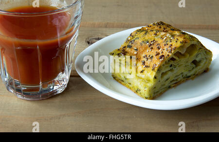 Spinat und Käse Kuchen mit einem Glas Tomatensaft auf einem Holztisch Stockfoto