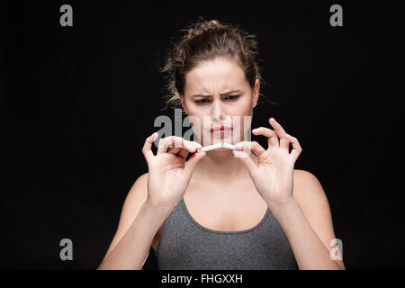 junge Frau bricht eine Zigarette, Rauchen Konzept auf schwarzem Hintergrund Stockfoto