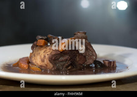 Coq Au Vin auf Platte von Seite. Klassische französische Gericht zubereitet Huhn in Rotwein mit Gemüse serviert Stockfoto