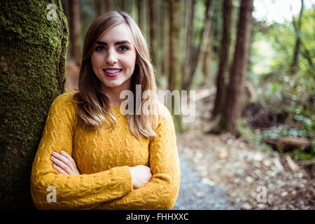 Hübsche blonde Frau, die an einen Baum gelehnt Stockfoto