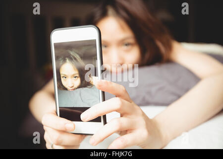 Brünette nehmen Selfie auf dem Bett liegend Stockfoto