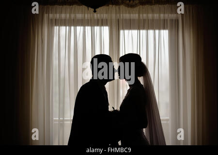 Silhouetten von Braut und Bräutigam auf dem Hintergrund eines Fensters Stockfoto