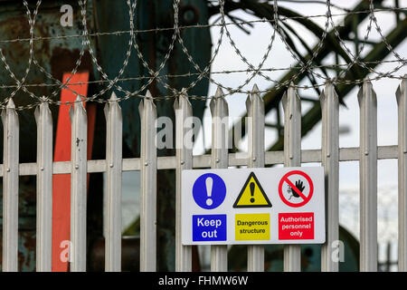 Metall-Zaun, Stacheldraht und Warnschilder an der Außenseite eines geschlossenen Industriegeländes, in der Nähe von Glasgow, Scotland, UK Stockfoto