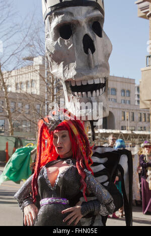 Eine riesige Schädel Marionette grins toothily hinter einer Frau, gekleidet in einem bunten Kostüm in Asheville Karneval parade Stockfoto