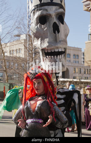 Eine riesige Schädel Marionette grins toothily hinter einer Frau, gekleidet in einem bunten Kostüm in Asheville Karneval parade Stockfoto