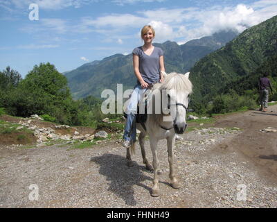 Cute blonde touristischen Mädchen auf dem Pferd trek nach Triund Indien die Ausläufern des Himalaya im Hintergrund Stockfoto