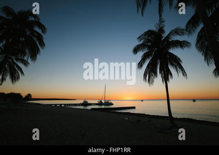 Ein helles orange Sonnenuntergang an einem kubanischen Strand mit den Silhouetten von Segelbooten und Palm Treets im mittleren Boden. Stockfoto