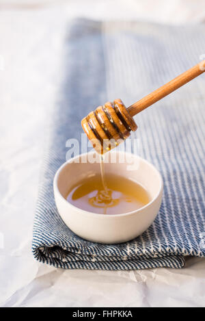 Ein leicht seitlicher Blick auf Honig wird von einem Honig-Stick in eine kleine Schüssel beträufelt. Stockfoto